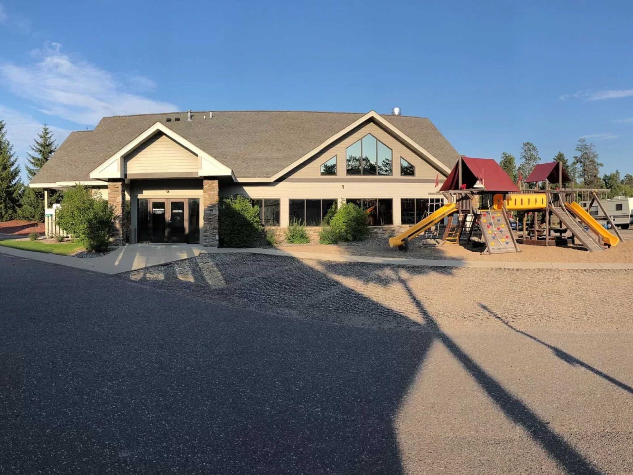 A two-story building with a large entrance, a playground with slides, and a gravel driveway.
