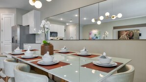 Een moderne eetruimte met een glazen tafel, witte stoelen en een grote spiegel erboven.
