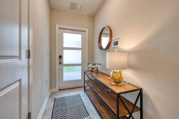 A hallway with a wooden bench, a wall-mounted mirror, a lamp, and a door with frosted glass panels.