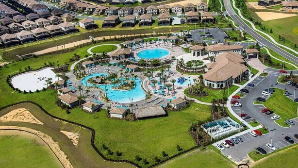 An aerial view of a resort with multiple swimming pools, a parking area, and a golf course. - Stylish 2BR Condo | Avengers Room & Golf Course View (Kissimmee)