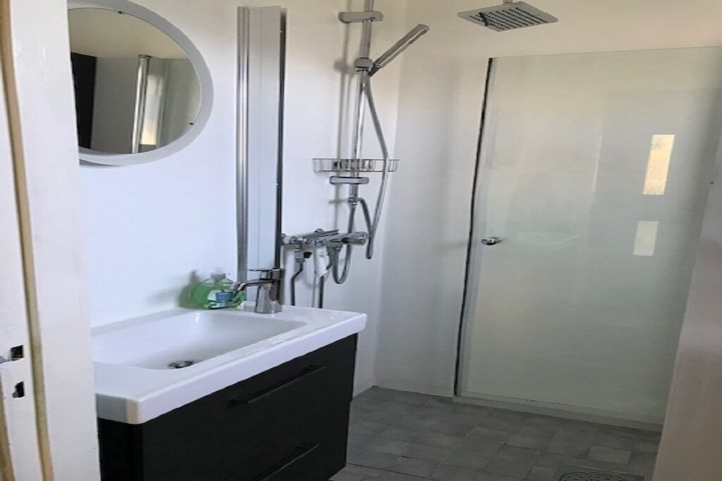 A bathroom with a white sink, dark cabinet, and a glass shower enclosure.