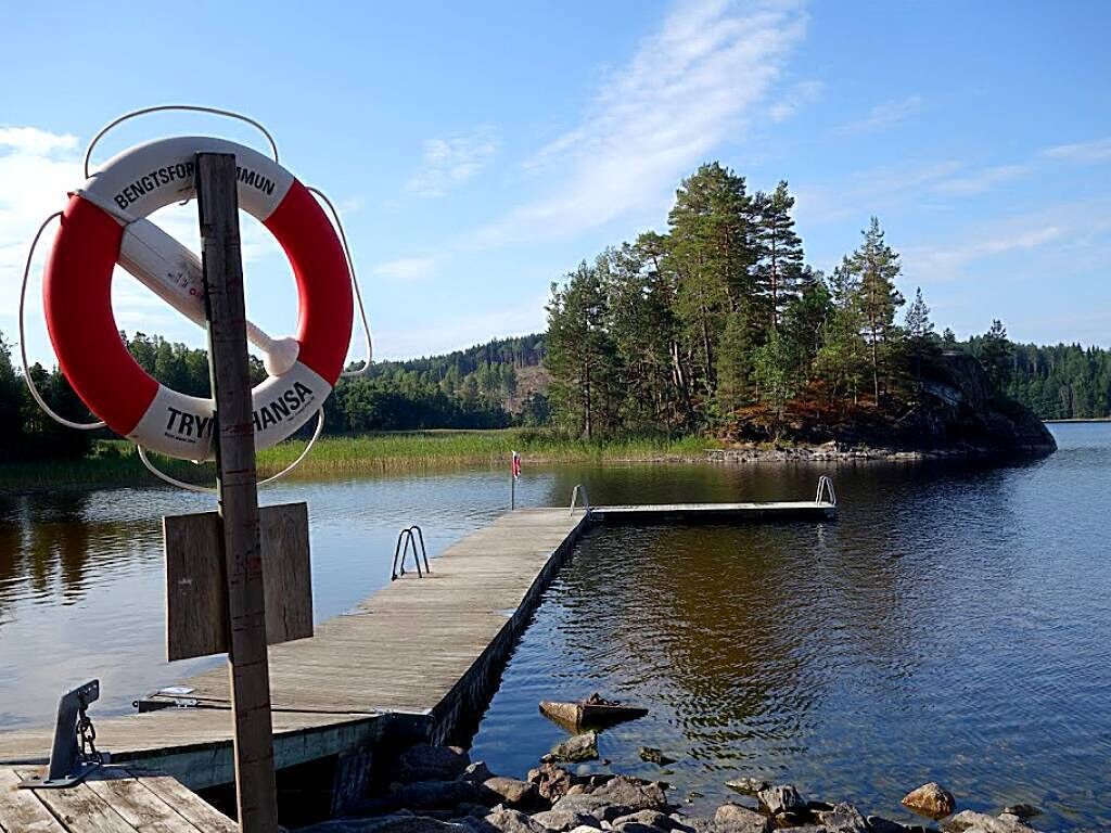 A wooden dock extending into a calm lake with a lifebuoy attached to a pole.