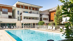 A swimming pool with lounge chairs, a multi-story building with balconies, and a clear sky. - Apartment - Terrasses De L'Océan with Shared Pool, Wi-Fi, and Air Conditioning (MOLIETS et MAA)