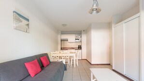 A compact living space with a sofa, a dining table, and a kitchenette in the background. - Apartment - Terrasses De L'Océan with Shared Pool, Wi-Fi, and Air Conditioning (MOLIETS et MAA)