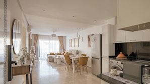 Cozinha moderna com forno embutido, área de jantar com mesa e cadeiras, e sala de estar com sofá e mesa de centro.