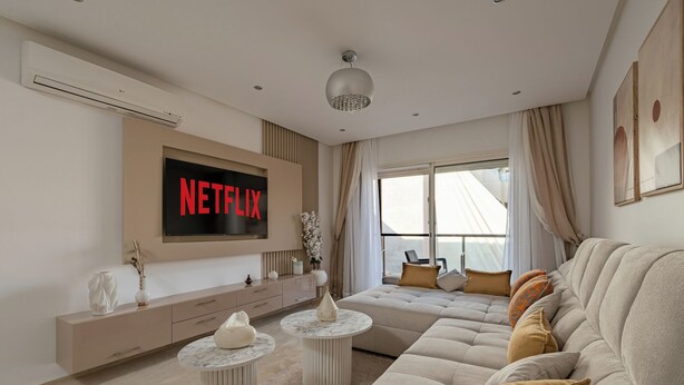 Un salon moderne doté d’un grand t éléviseur à écran plat affichant le logo « NETFLIX », d’un canapé beige, d’une table basse et d’un buffet.