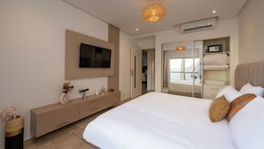 Une chambre moderne avec un grand lit, un téléviseur fixé au mur, une table de chevet avec une lampe et une armoire avec un miroir.