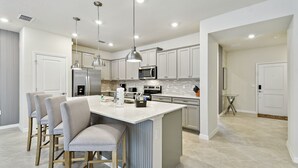 Una cocina moderna con una isla central, taburetes de bar, electrodomésticos de acero inoxidable e iluminación colgante.