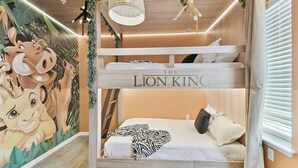 Una cama litera con un mural de personajes de 'El Rey León', un ventilador de techo y una ventana con persianas.