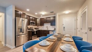 Una cocina moderna con electrodomésticos de acero inoxidable, armarios de madera oscura y un comedor con sillas azules y una mesa de madera.