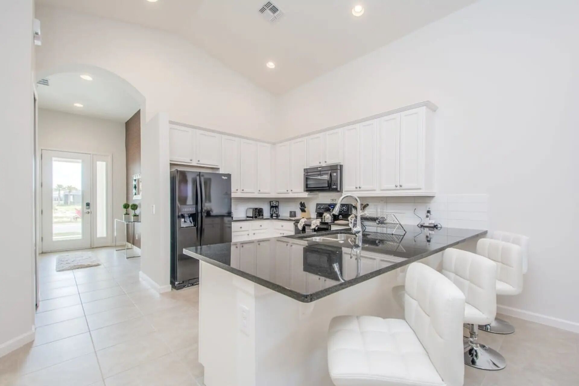 Una cocina moderna con armarios blancos, un refrigerador de acero inoxidable, un microondas y una isla central con taburetes de bar.