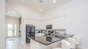 A modern kitchen with white cabinetry, a stainless steel refrigerator, a microwave, and a central island with bar stools. - Private Pool Home in Bella Vida Resort (Kissimmee)