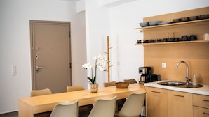 A modern kitchen with a wooden table, chairs, a sink, and a shelf with dishes. - WHITE LUXURY APARTMENT (Trikala)