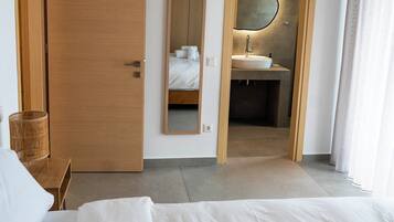 Ein Hotelzimmer mit einem großen Bett, einer Holztür, einem Spiegel und einem durch eine geöffnete Tür einsehbarer Badezimmer.