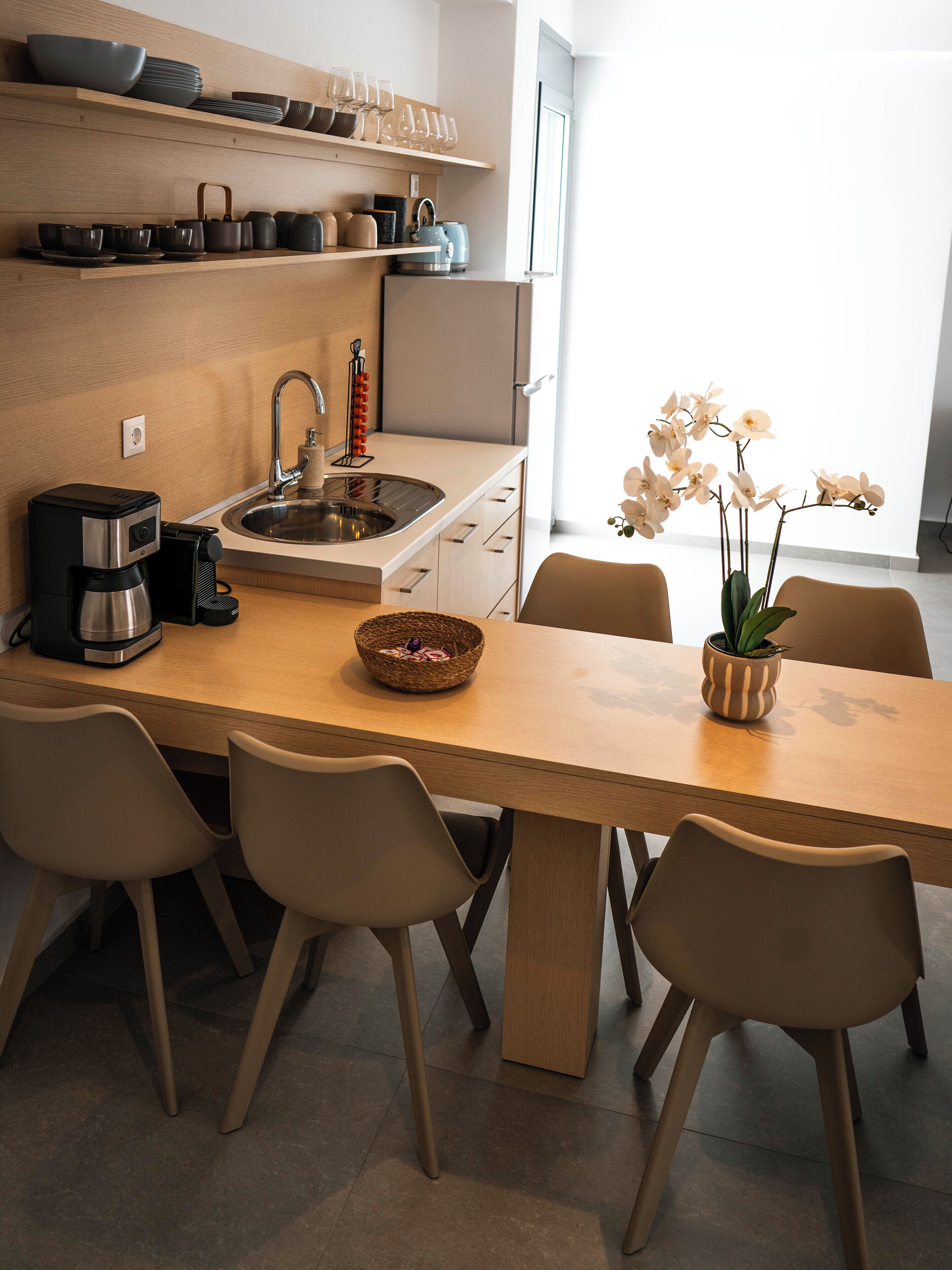 Une cuisine moderne avec un plan de travail en bois, une machine à café et un évier. Des chaises sont disposées autour de la table, et un vase rempli de fleurs y est posé.