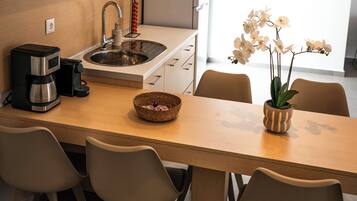 Une cuisine moderne avec un plan de travail en bois, une machine à café et un évier. Des chaises sont disposées autour de la table, et un vase rempli de fleurs y est posé.