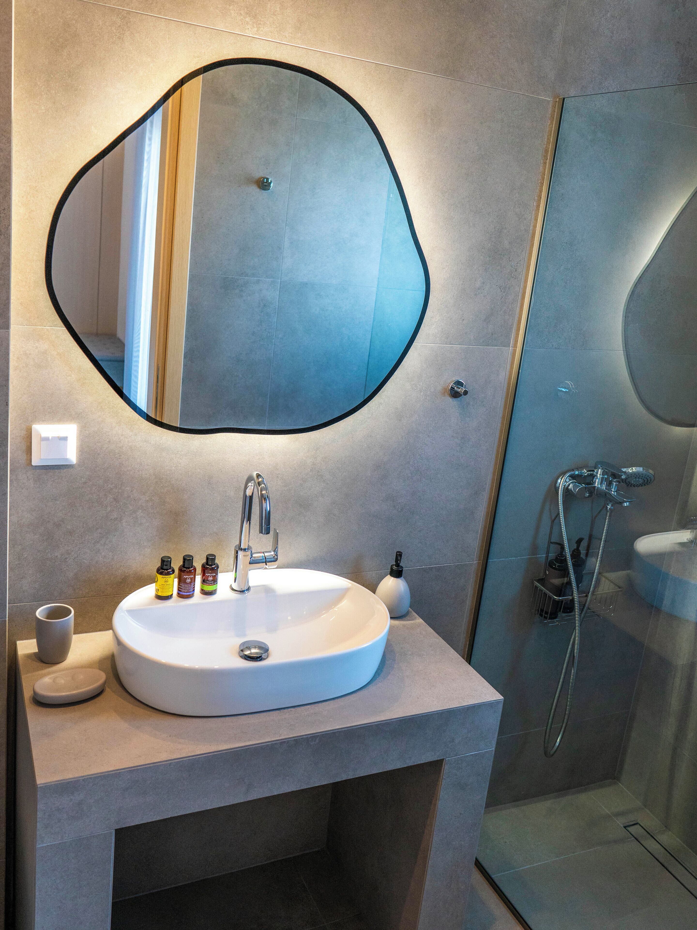 Un bany modern amb un mirall oval gran, un lavabo blanc i una dutxa amb portes de vidre.