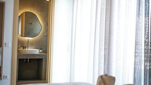 A hotel room with a bed, a bathroom with a sink, a mirror, and a window with curtains. - WHITE LUXURY APARTMENT (Trikala)