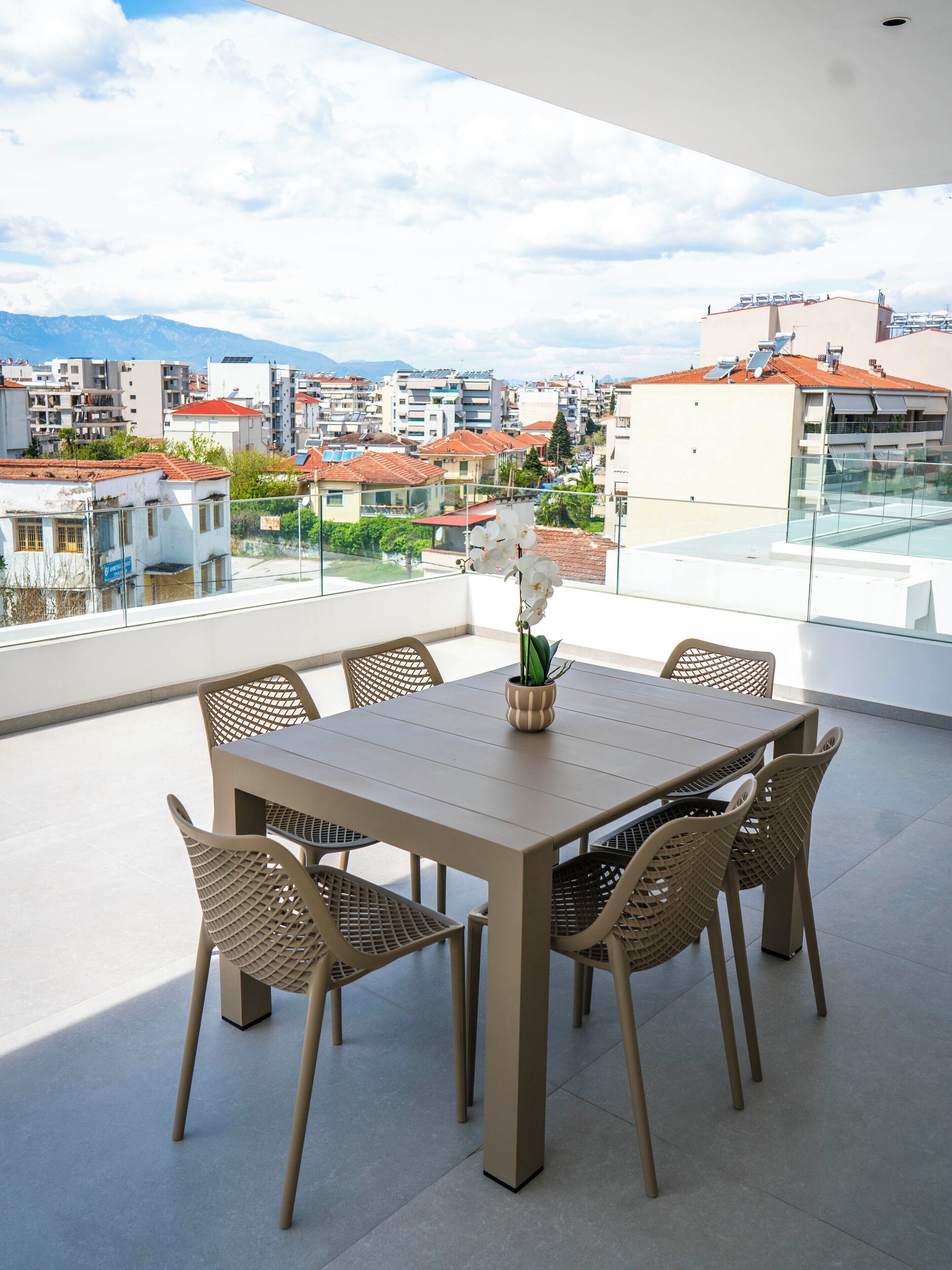Een moderne buiten eethoek met een glazen balustrade, een houten tafel en rieten stoelen.