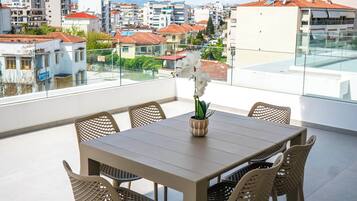 Een moderne buiten eethoek met een glazen balustrade, een houten tafel en rieten stoelen.