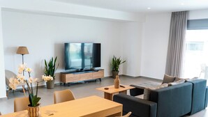 A modern living room with a sofa, a TV, a dining table with chairs, and potted plants. - WHITE LUXURY APARTMENT (Trikala)