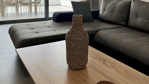 A modern living room with a sofa, a wooden coffee table, and a view of buildings and mountains through large windows. - WHITE LUXURY APARTMENT (Trikala)