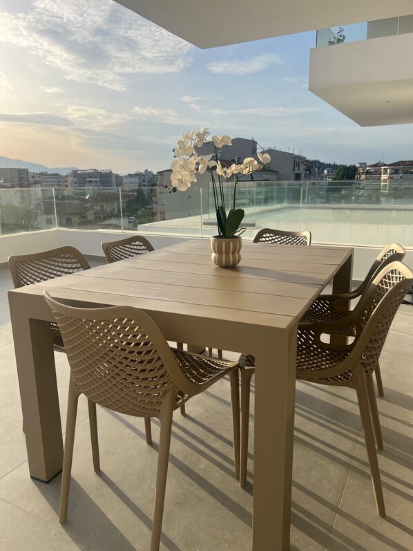 A rooftop terrace with a table and chairs, a potted orchid, and a city view. - WHITE LUXURY APARTMENT (Trikala)