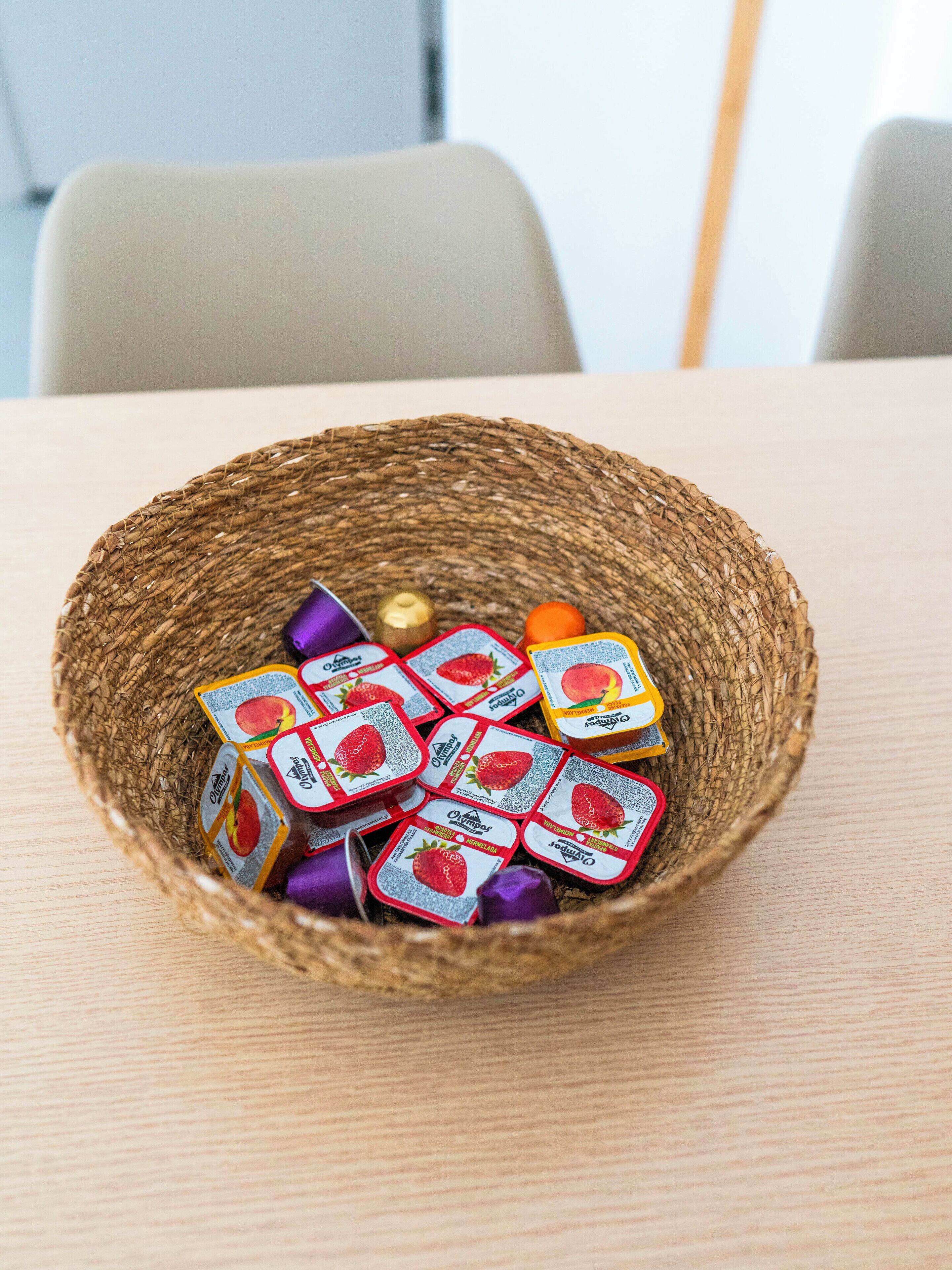Ein geflochtener Korb, gefüllt mit verpackten Lebensmitteln, auf einer Holztischplatte.