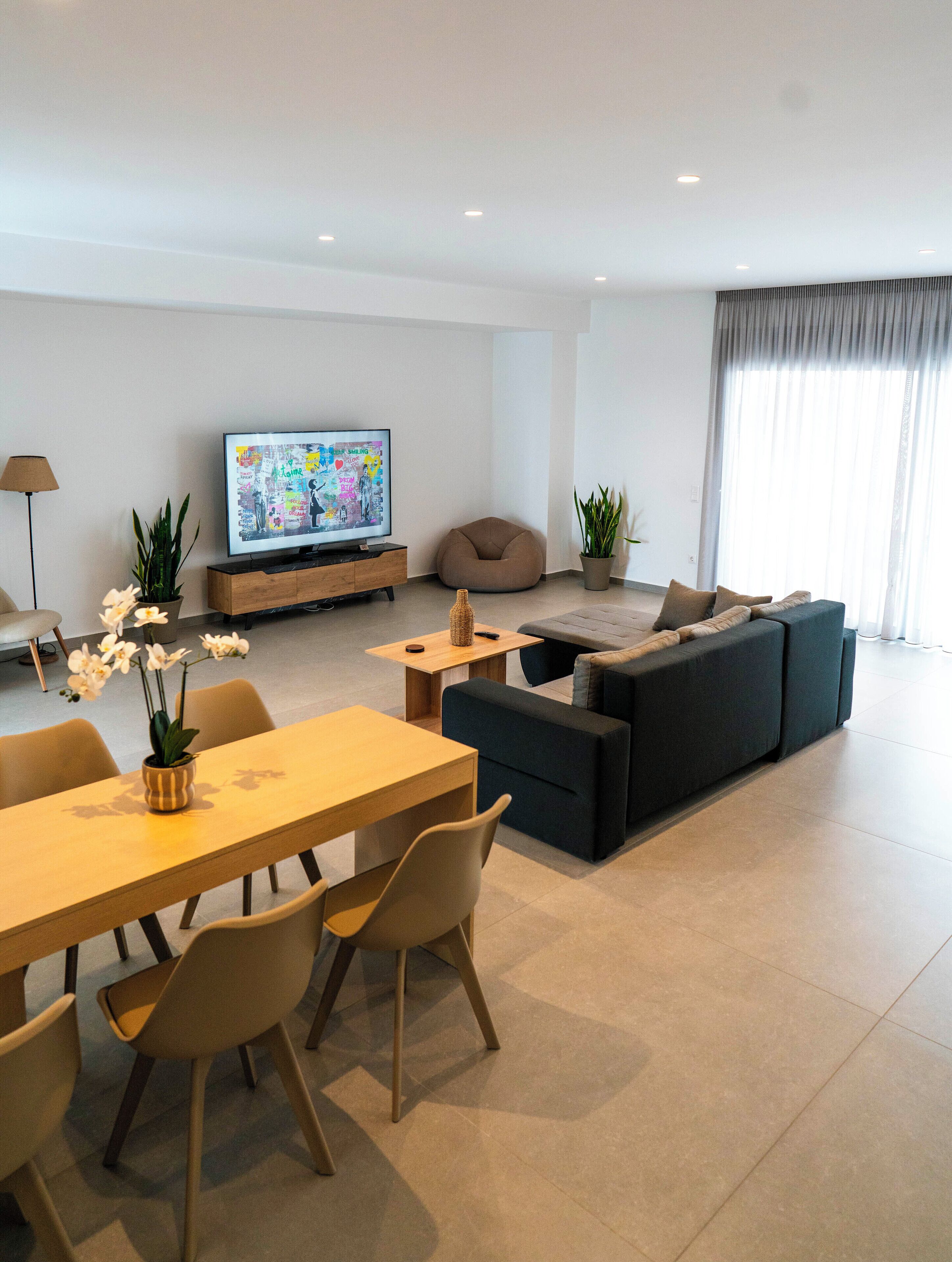 A modern living room with a sofa set, a dining table with chairs, a TV, and a potted plant.