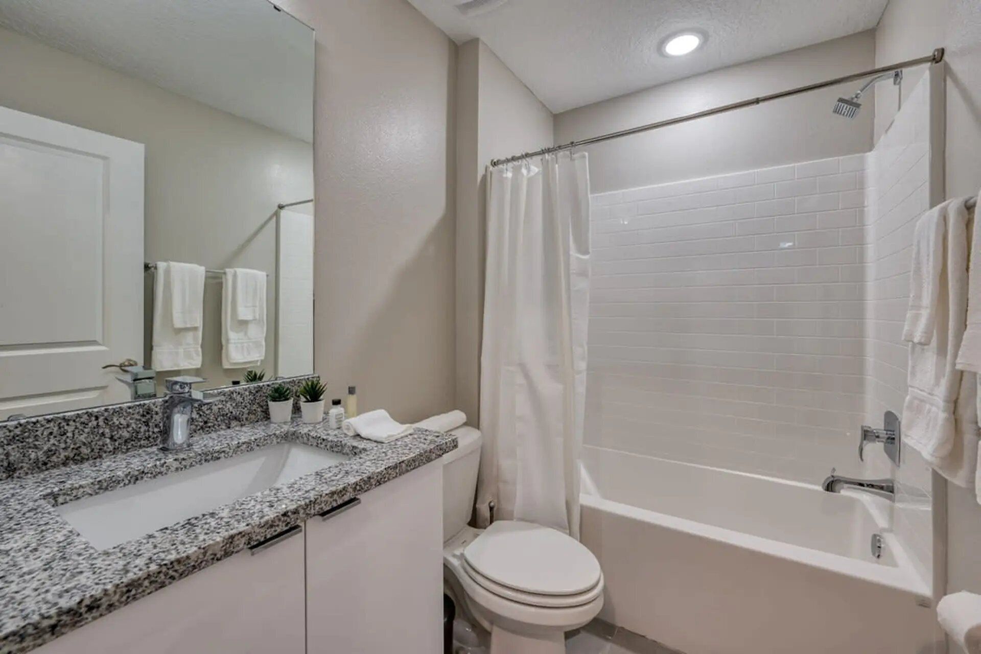 Une salle de bain avec des toilettes blanches, un lavabo doté d’un plan de travail en granit et une baignoire avec un rideau de douche.