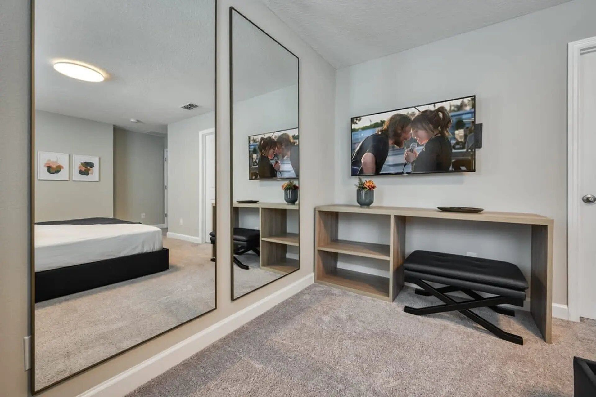 Une chambre à coucher moderne avec un lit, un grand miroir, une télévision et une console sur laquelle est posé un vase.