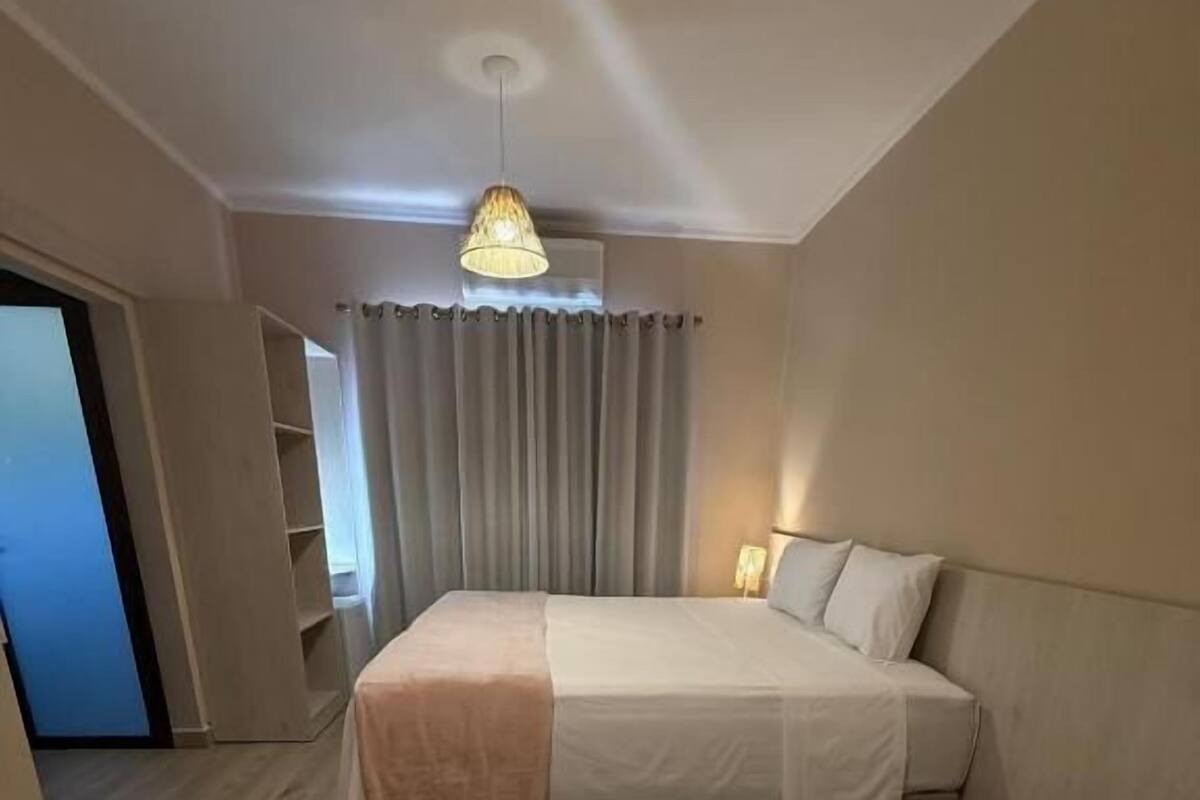 A hotel room with two beds, a ceiling light, a window with curtains, and a door leading to another room.