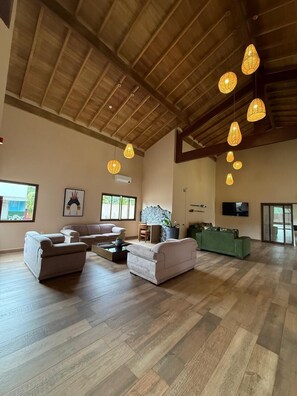 A spacious living room with a high wooden ceiling, multiple sofas, a coffee table, and pendant lights.