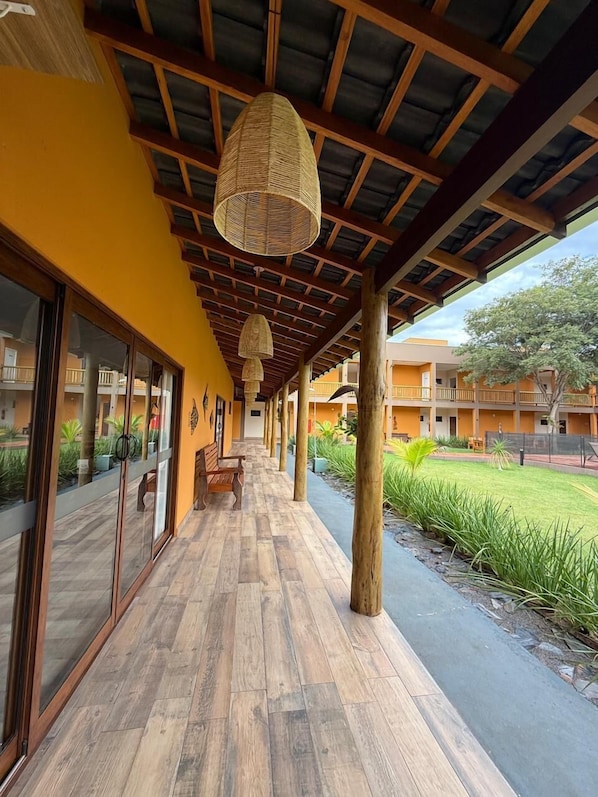 A covered walkway with wooden flooring, large windows, and hanging lamps.