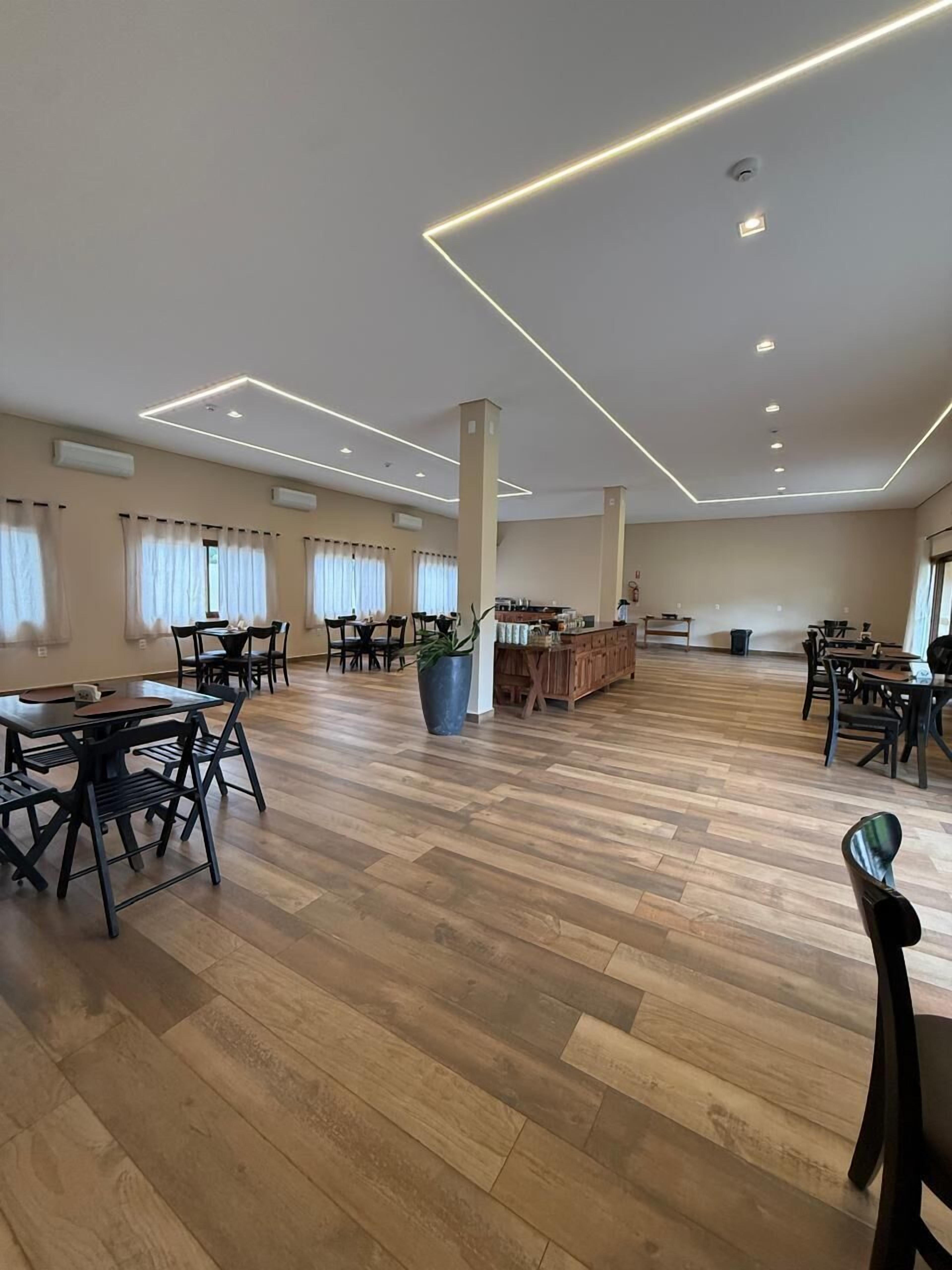 Un vaste espace dédié à la salle à manger, doté d’un plancher en bois, de plusieurs tables et chaises, et agrémenté d’une plante au centre.