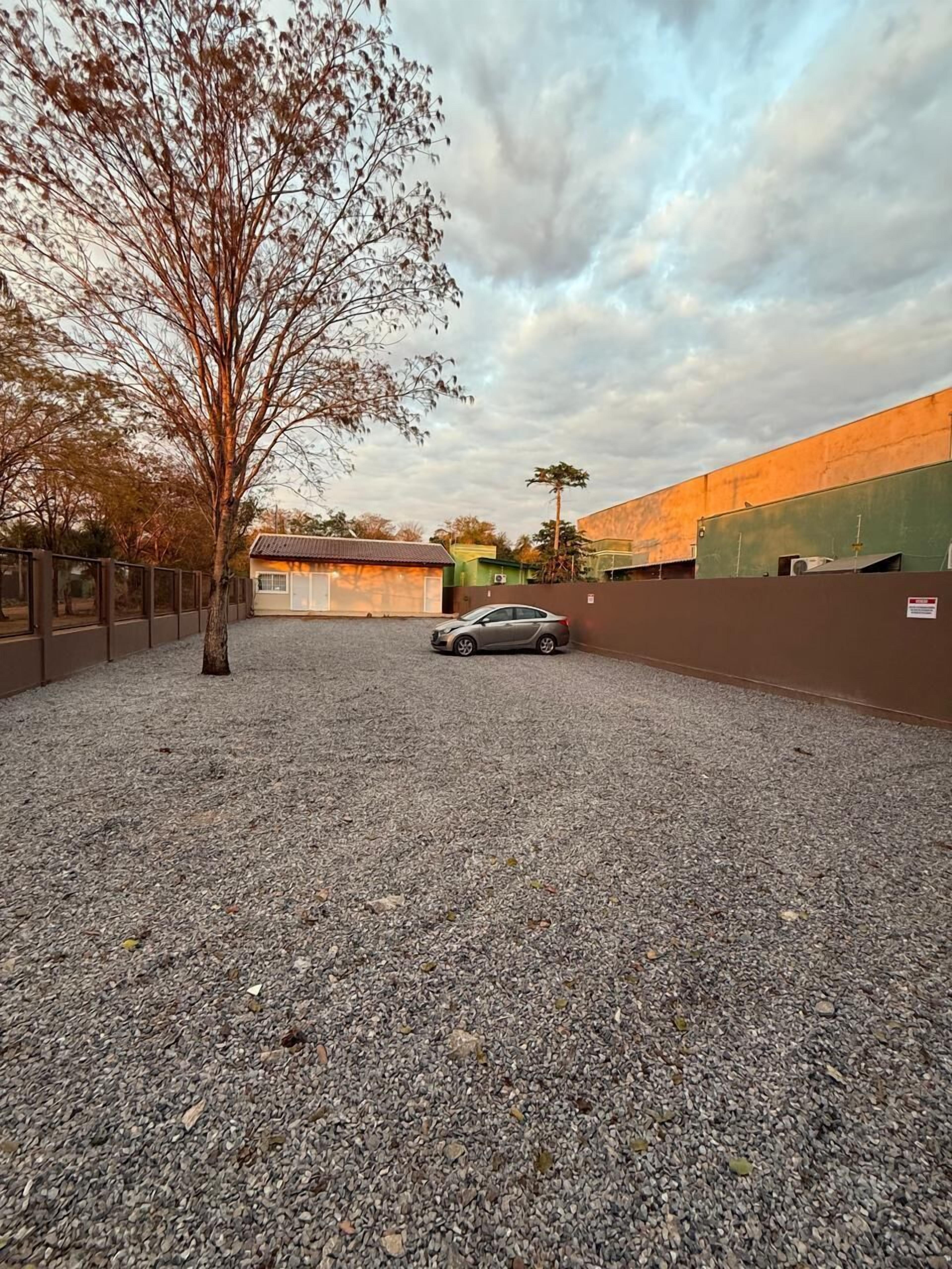 A gravel parking area with a car, a tree, and industrial buildings in the background.