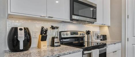 A compact kitchen with white cabinets, a built-in microwave, a coffee maker, and a kettle.