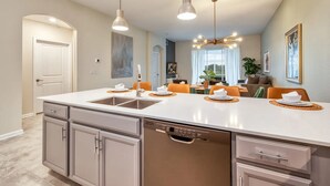 Une cuisine moderne dotée d’un grand îlot central, d’un lave-vaisselle intégré et de luminaires suspendus.