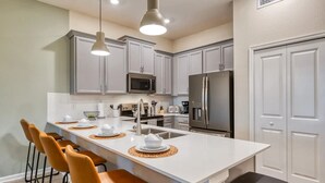 Une cuisine moderne avec des meubles blancs, des appareils en acier inoxydable et un îlot central doté de tabourets de bar.