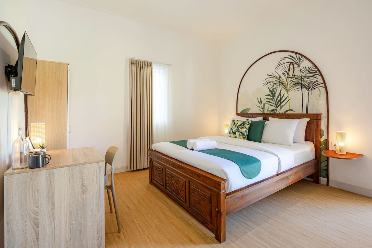 Un dormitorio ordenado con una cama de madera, una mesita de noche con una lámpara, un escritorio con una silla y un espejo grande en la pared.