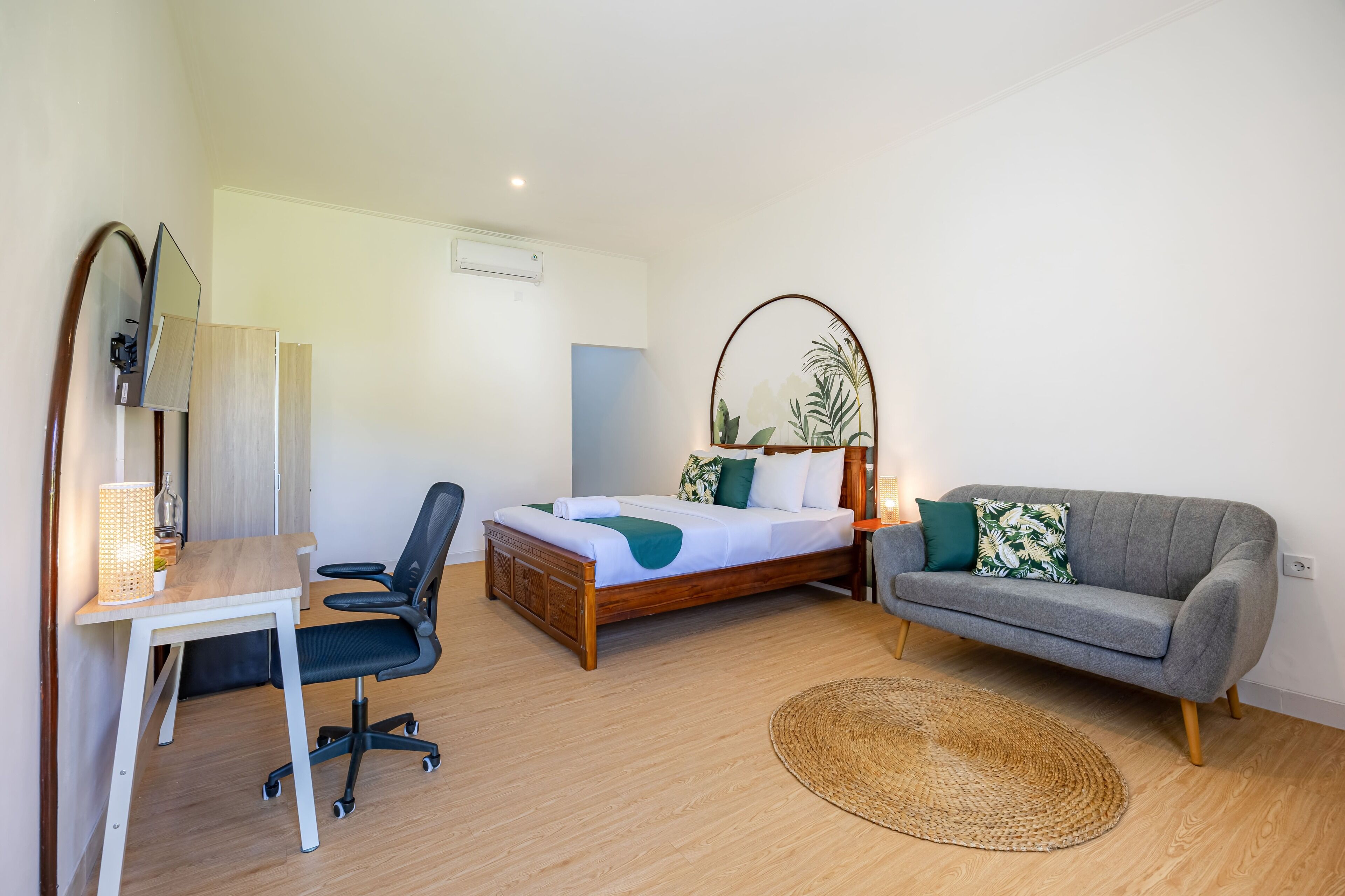 Un dormitorio con cama, escritorio, silla, sofá y alfombra redonda.
