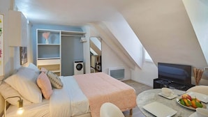 A modern loft bedroom with a bed, a TV, a dining area, and a laundry machine. - Lovely Studio Place Vendome Opera (Paris)