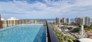 Ein Pool auf dem Dach mit Blick auf die Stadt, umgeben von Hochhäusern und Palmen.