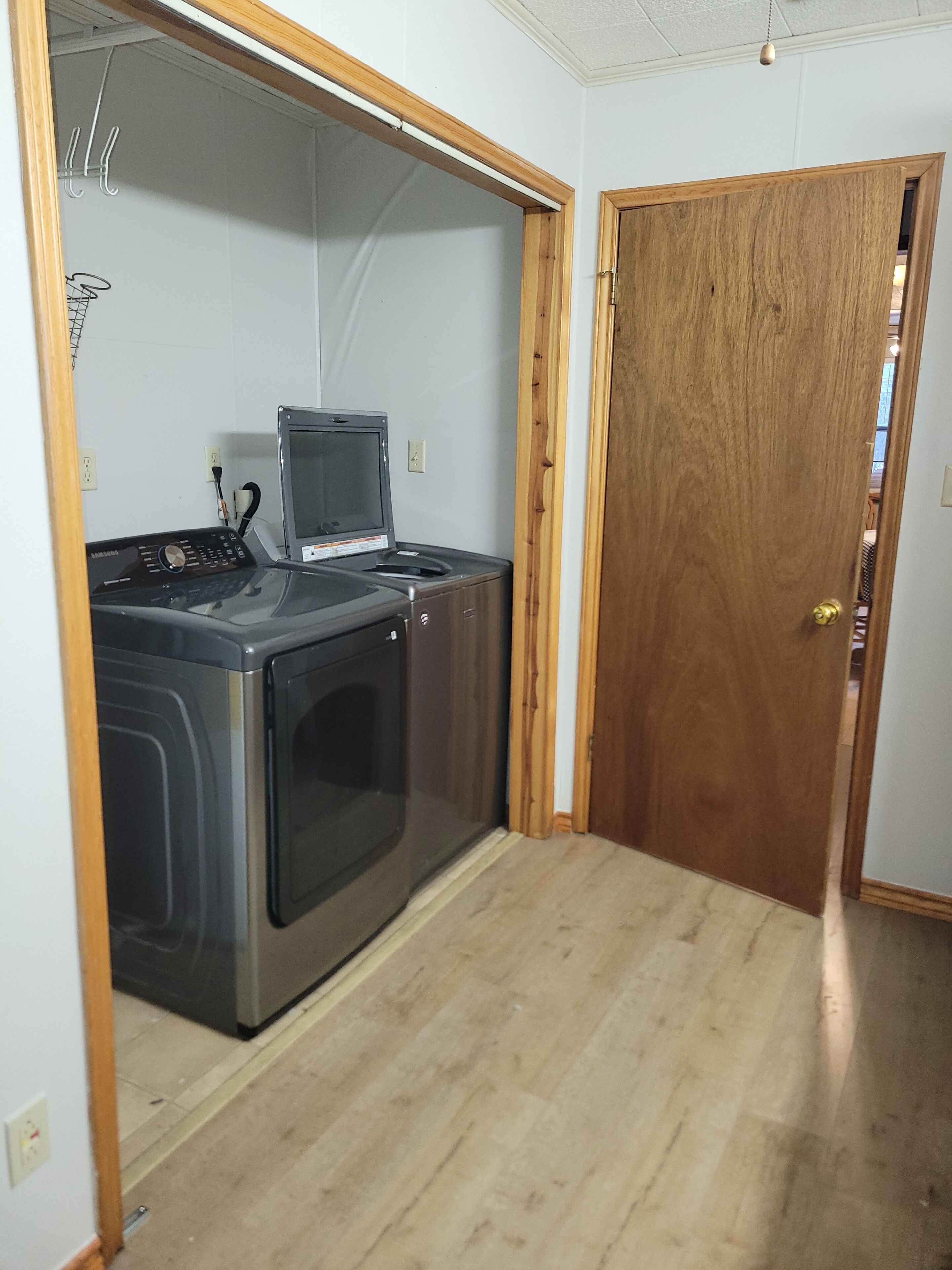 A compact laundry room with a washing machine and dryer, a wooden door, and a light switch on the wall.