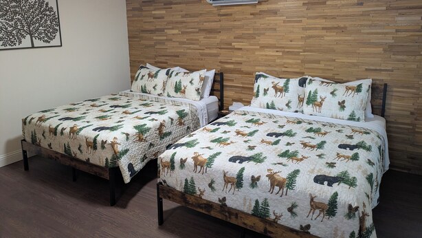 Two beds with a forest-themed bedding, a wooden headboard, and a wall-mounted air conditioner. - South of the Border Lodging (Canaan)