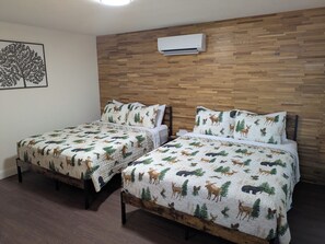 Zwei Betten mit Waldmotiv auf der Bettwäsche, ein hölzernes Kopfende und eine Wand-Klimaanlage.