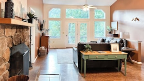 A spacious living room with a fireplace, a large window, and a ceiling fan.
