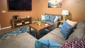 A living room with a flat-screen TV, a sofa, a coffee table, and a painting on the wall.