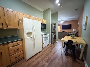 A compact kitchen with wooden cabinets, a refrigerator, a microwave, and a washing machine.