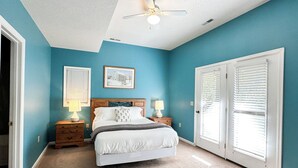 A bedroom with a bed, two bedside tables with lamps, a ceiling fan, and a window with blinds.